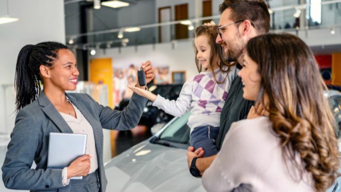 Used car dealer giving key to family for their new car.