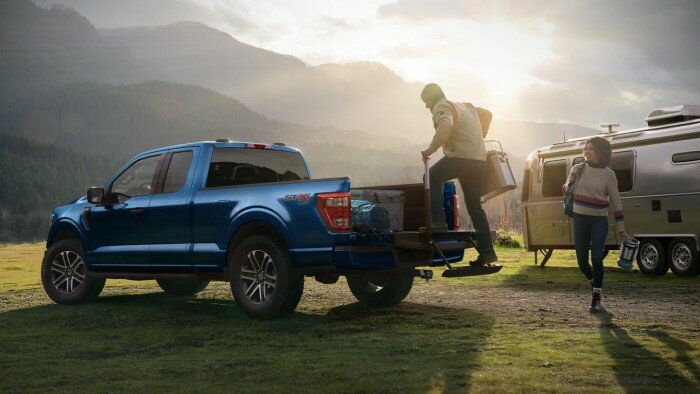 Blue Ford F-150 parked off-road next to a camper.