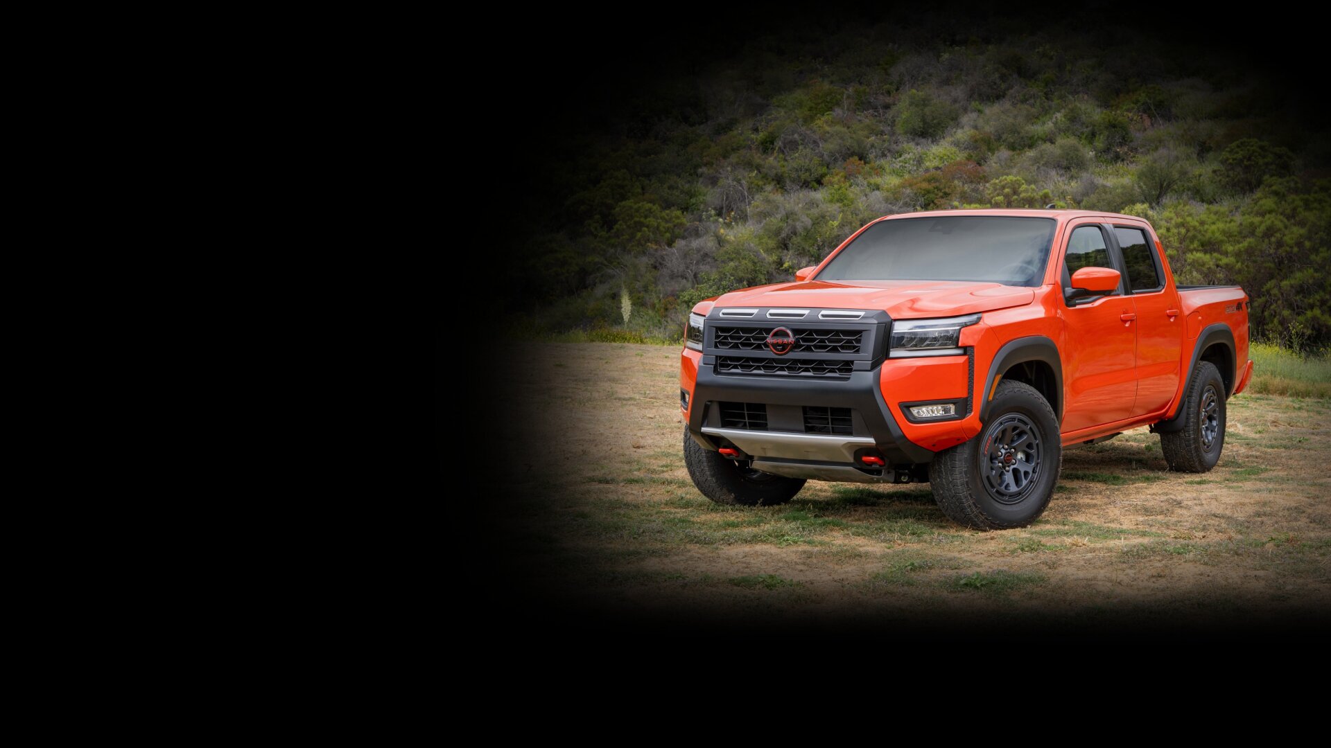 Front grille view of an Orange Nissan Frontier parked off-road.